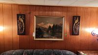 Overall view of framed landscape print centered between two bird relief plaques on wood panel wall