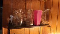 Shelf with four clear glass vases and pink plastic tumbler