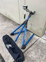 Full view of blue Park Tool PRS-5 stand folded with carry bag on ground