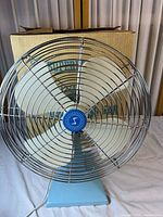 Front view showing fan face, blades, cage and base with box behind