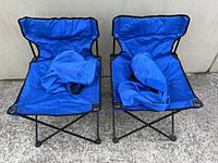 Two blue folding chairs with carry bags displayed on ground