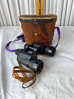 Binoculars resting against brown leather case showing overall lot