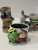 Front view of frog planter with piano, donkey planter, owl planter in background