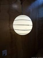 full view of illuminated white glass globe with gold rings suspended from rod