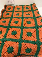 Full view of folded orange and green crochet blanket showing square motif