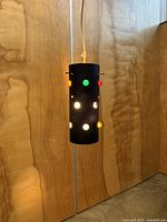 Full view of black cylindrical pendant light illuminated, coloured jewel lenses visible