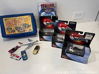 Group shot of all items: three boxed Hot Wheels 100%, four loose cars, jet airliner, blue Car Case