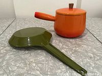 Top view of olive green frying pan and orange sauce pan with lid