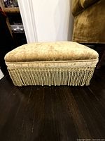 Full view of rectangular gold velvet ottoman with fringe