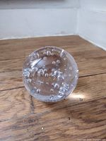 Spherical clear glass paperweight on wood floor showing internal bubbles
