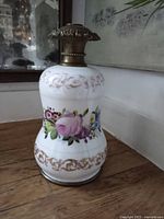 Front view of milk glass oil lamp base with floral hand-painted design and brass collar