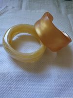 Two lucite bangles, cream marbled and peach sculpted, on cloth
