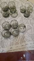 Twelve smoky gray glasses in three sizes displayed on towel