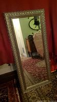 Full view of the mirror leaning against wall showing entire ornate frame and beveled glass