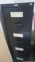 Front view of matte black 4-drawer filing cabinet showing handles, label frames and lock cylinder