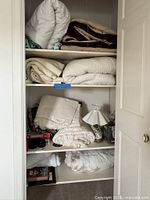 Closet shelves showing folded linens, lamp, board game and decor items