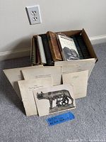 Box with books upright and several prints leaning in front, showing quantity and condition