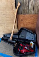Chainsaw in case and broad axe leaning beside