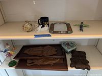 Overall shot showing all items on two shelves: stained-glass mirror, ceramic pieces, wood carvings, butterfly sculpture, mug, cross, trinket box