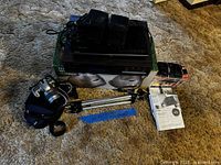 Group view of all items: Nikon camera with bag, tripod, speaker set box with speakers, Blu-ray and VHS players, Sharp organizer box