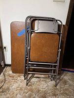 Two brown folding card tables and stacked brown vinyl folding chairs