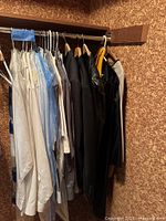 Clothing rack with multiple men’s suits, trousers and dress shirts on hangers, some in dry-cleaner bags