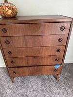 Front view of walnut tallboy dresser showing five drawers, pulls, legs
