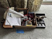Overview of box containing change tray, dog figurine, suspenders, gyroscope, linens, buttons and other small items