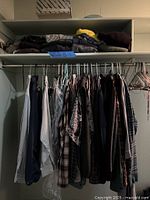 Closet view showing hanging shirts, jackets, trousers and folded apparel on upper shelf with hangers visible