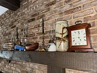 Overview of mantel showing clock, lamps, candlesticks, books, stoneware jar, wood bowl and jug