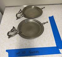 Overhead view of two matching pewter sconces showing backplates, arms and candle cups