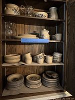 Cabinet shelves showing multiple Pfaltzgraff Yorktowne stoneware dinnerware and serveware pieces and two clear glass carafes