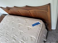 Headboard behind mattress showing scalloped top, wood tone, right leg chip, mattress surface