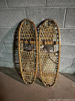 Pair of traditional wooden snowshoes leaning against wall showing full frames and webbing