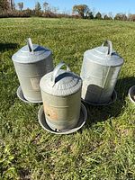 Three galvanized poultry waterers on grass showing size comparison