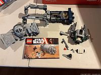 Instruction manual, minifigure parts, partially built grey ship sections and escape pod pieces on table