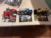 Four partially assembled Technic vehicles on their manuals with loose parts bag in background