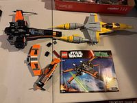 Overview showing booklet, black-orange X-Wing sections, gray-yellow starfighter, orange craft, loose bricks