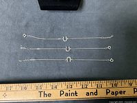 Three sterling silver horseshoe bracelets laid flat beside ruler