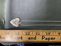 Heart locket pendant and partial chain beside ruler