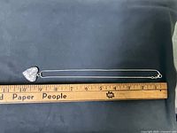 Chain fully extended beside ruler showing length, heart locket at one end, clasp at other, confirming scale and metal colour