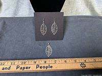 Full view of earrings on card with pendant below alongside ruler for scale