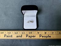 Ring in open box against ruler showing scale