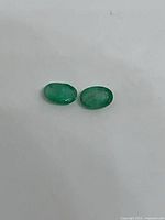 Pair of oval green emeralds on white background
