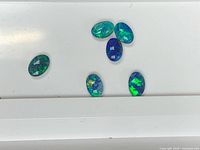 Six oval opal doublets on white surface