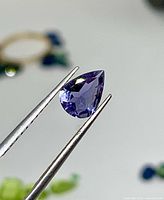 Front view of pear-shaped vivid violet iolite held by tweezers