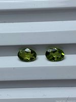 Two oval faceted olive green peridot stones on white surface