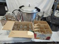 Full lot view showing both pressure cookers, enamel pot, jam jar cartons, and quart jars