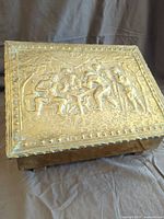 Lid of brass box showing embossed tavern scene and patina