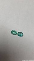 Two loose green emeralds, oval and cushion cuts on neutral background